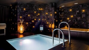 A modern indoor pool area with a clear pool, a lounge chair, and a wall with square tiles and embedded lights. - Hotel Soho Boutique Granada (Granada)