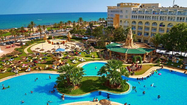 Un resort con varias piscinas, palmeras y un edificio grande con balcones.
