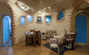 Une pièce dotée d’un plafond en pierre rustique, d’un fauteuil de massage, d’une table de massage, d’une petite table avec une bouteille et d’une chaise avec un panier.