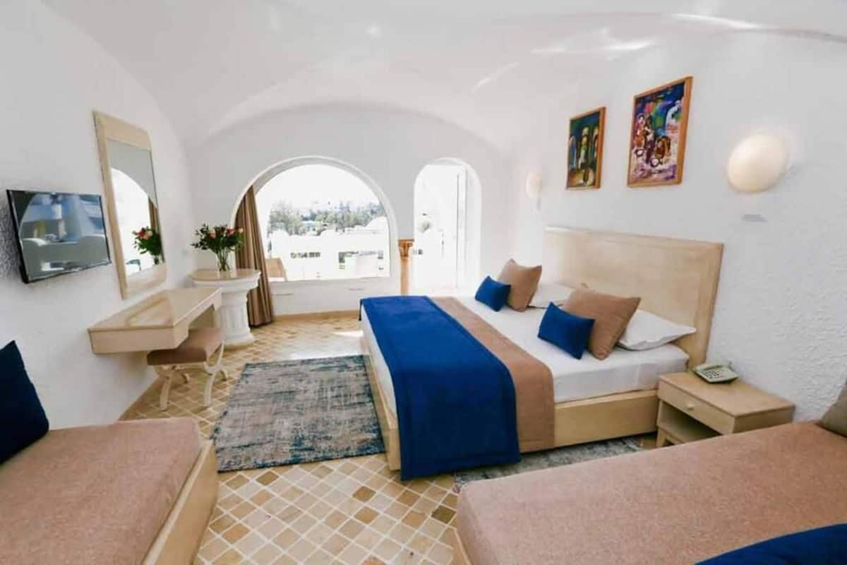 A hotel room with a bed, bedside table, TV, and a view through an arched doorway.