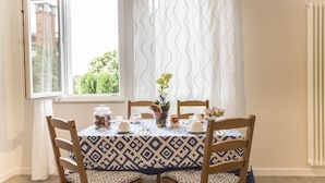 Zona pranzo con tavolo apparecchiato per quattro, circondata da sedie in legno con cuscini decorati.
