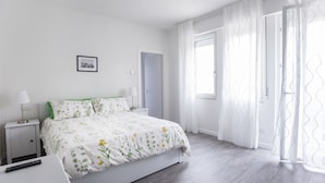 Una camera da letto con un letto, comodini, un quadro incorniciato, una finestra con tende e una porta.