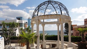 A gazebo with a dome roof, surrounded by potted plants and palm trees, overlooking a body of water with buildings in the background. - Vox Maris Grand Resort - Adults only (Costinesti)