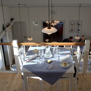Un comedor con una mesa dispuesta para dos personas, con mantel azul, sillas blancas y barandilla de madera.