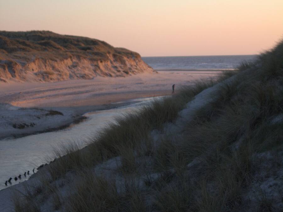 Una playa con dunas de arena y una persona caminando.