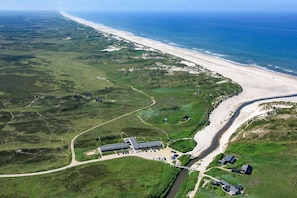 Vista aérea de una zona costera con playa, un edificio grande con estacionamiento y un río.
