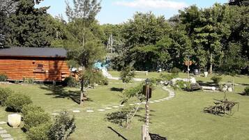 Una cabaña rústica con terraza de madera, rodeada por un jardín cuidado con un sendero sinuoso, bancos y diversas plantas.