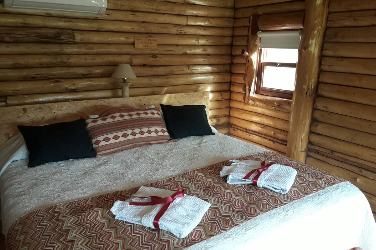 A wooden cabin room with a bed, pillows, a window, and a lamp.