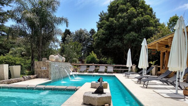 A pool with a waterfall feature, surrounded by lounge chairs and umbrellas, set in a landscaped garden with trees. - Pualy Resort & Spa (Loma Verde)