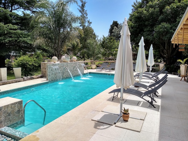 A swimming pool with a stone waterfall, lounge chairs, and umbrellas.