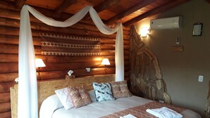 A wooden cabin bedroom with a four-poster bed, two wall-mounted lamps, and a stone wall. - Pualy Resort & Spa (Loma Verde)