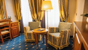 A hotel room with a wooden desk, two armchairs, a small round table, and a floor lamp. - Hotel Italia (Görlitz)