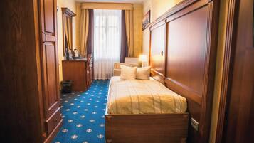A hotel room with a bed, a desk, a chair, a lamp, and a window with curtains.