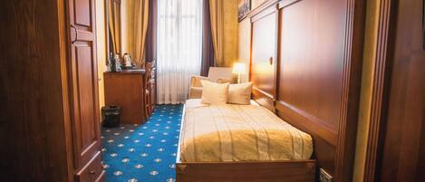 Ein Hotelzimmer mit Bett, Schreibtisch, Stuhl, Lampe und einem fenster mit Vorhängen.