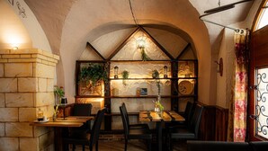 A restaurant with a stone wall, wooden tables, black chairs, and a decorative shelf with plants and lanterns. - Hotel Italia (Görlitz)