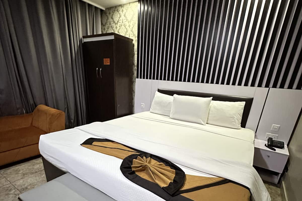 Ein modernes Hotelzimmer mit einem großen Bett, einem Nachttisch, einem Kleiderschrank und einem Sofa.
