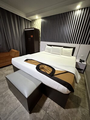 Una habitación de hotel moderna con una cama grande, una mesita de noche, un armario y un sofá.