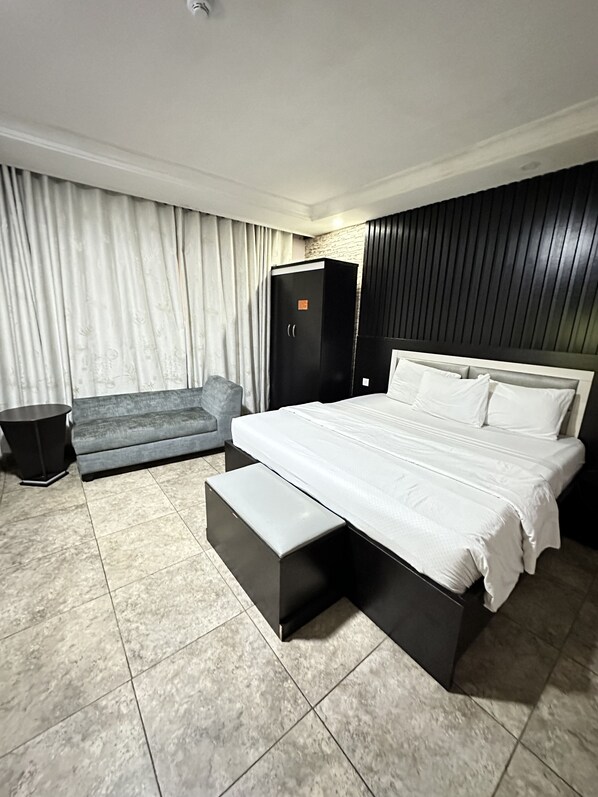 Una habitación de hotel moderna con una cama grande, un sofá gris, un armario negro y una mesita auxiliar pequeña.