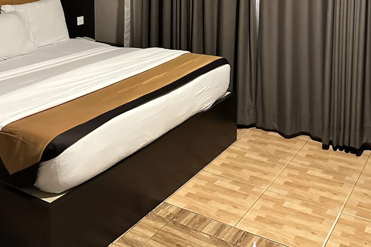 Ein Hotelzimmer mit einem großen Bett, dunklen Vorhängen, einem Holz-Kopfteil und einem Holzboden.