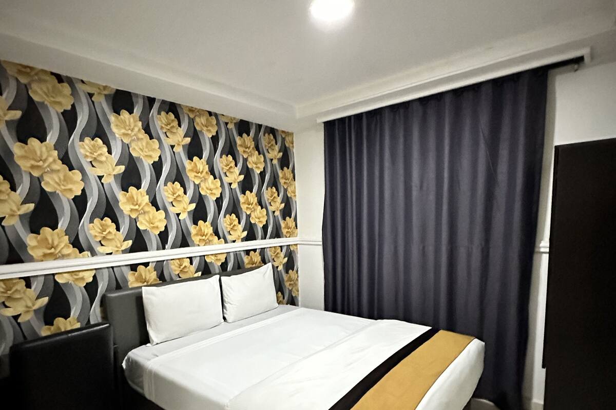 Ein modernes Hotelzimmer mit einem großen Bett, einem Nachttisch, einem Sessel und einem dunklen Vorhang.