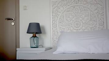 Una cama bien hecha con un almohadón blanco y una lámpara azul sobre una mesita de noche blanca.