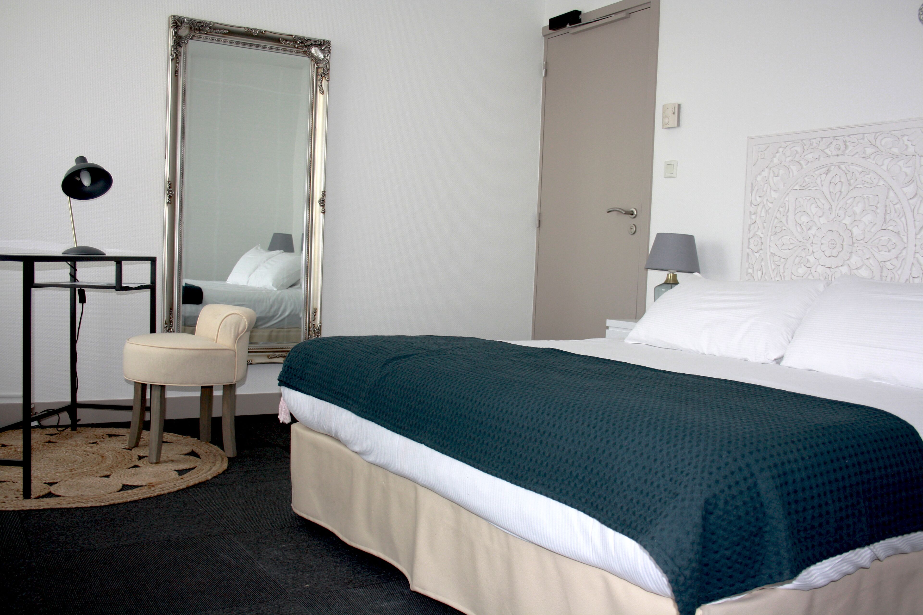 Una habitación de hotel ordenada con una cama, una silla, un escritorio con lámpara y un espejo grande.