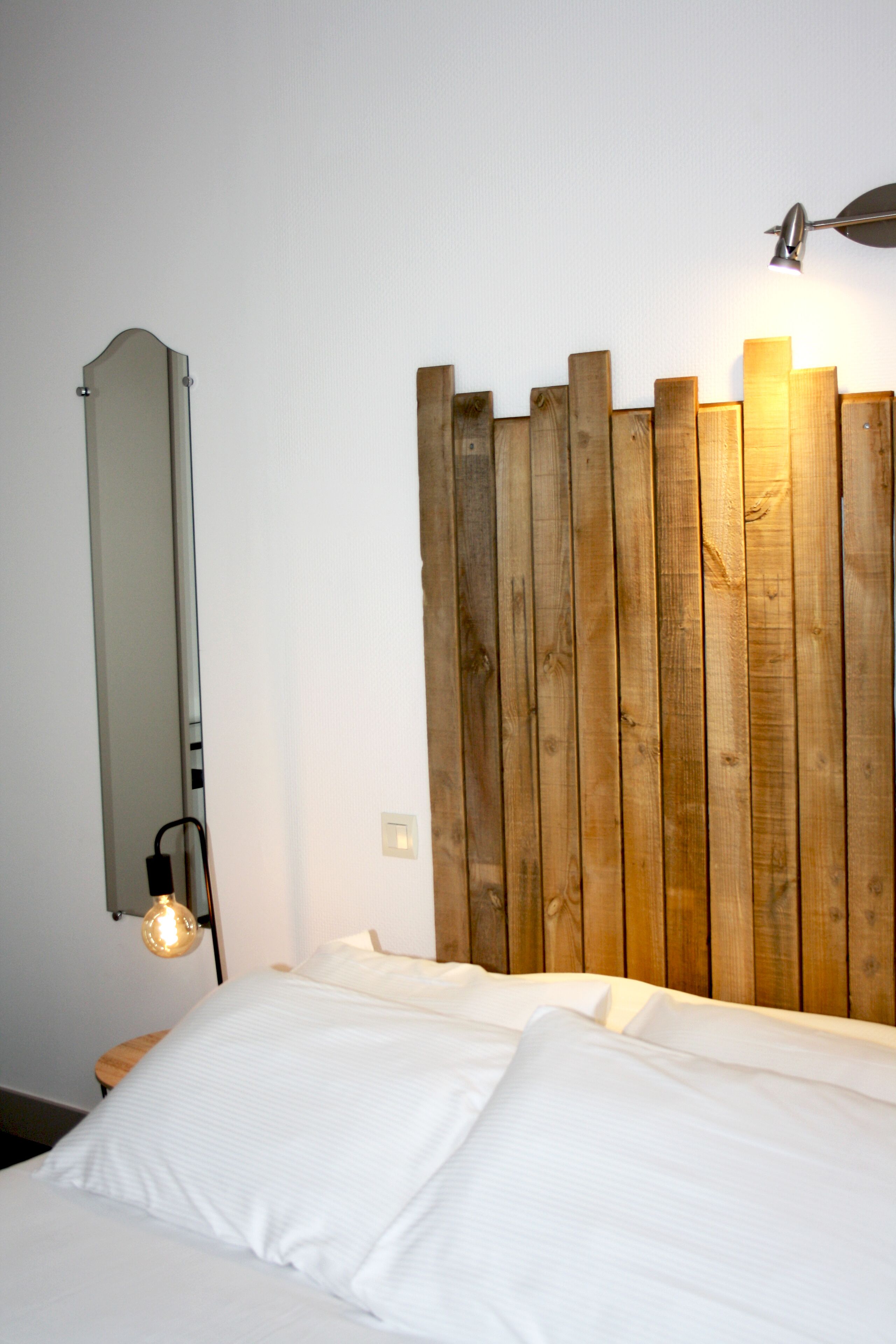 A bedroom with a wooden headboard, a bedside lamp, and a mirror on the wall.