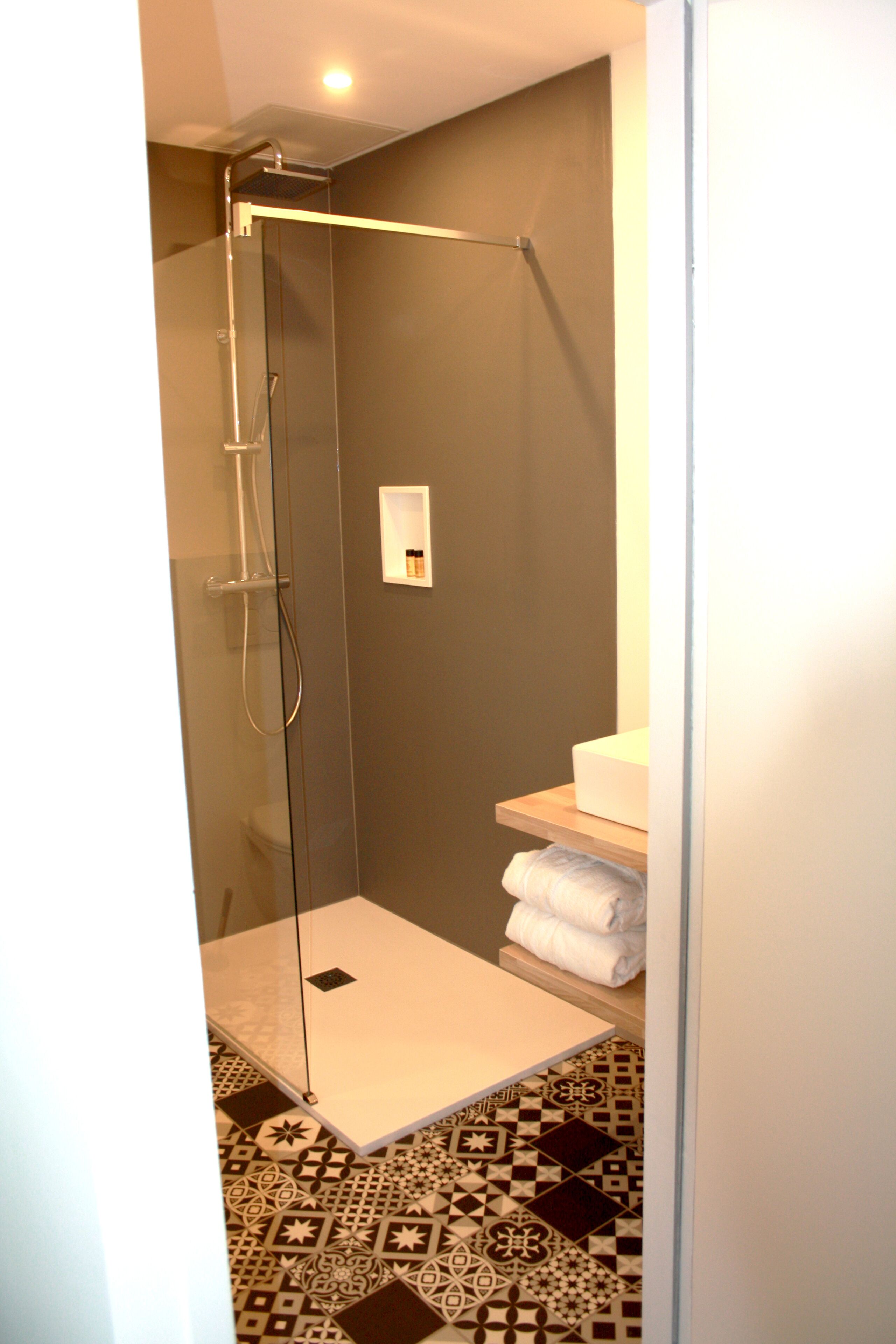 Ein modernes Badezimmer mit einer Duschkabine, einem weißen Waschbecken und fugenlosen Bodenfliesen.