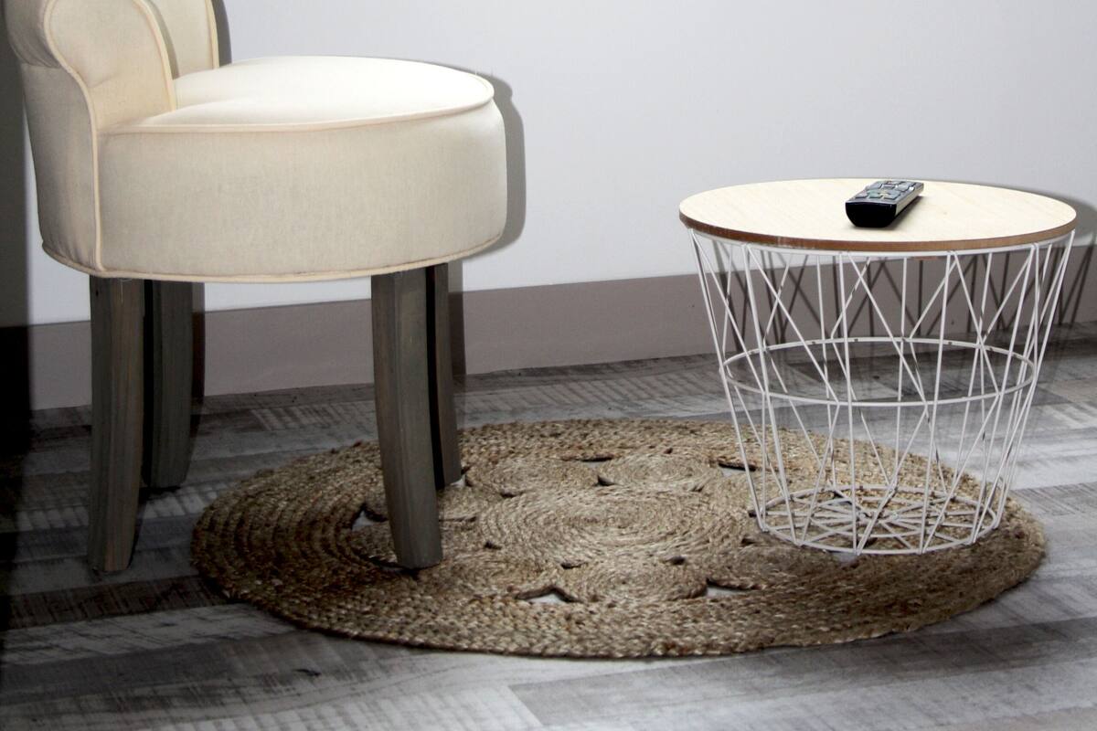 Une pièce comprenant une chaise, une table ronde avec un pied en fil de fer, un tapis tissé et une fenêtre avec des rideaux.