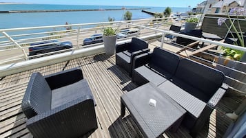 A deck with wicker furniture, a potted plant, and a view of the sea.