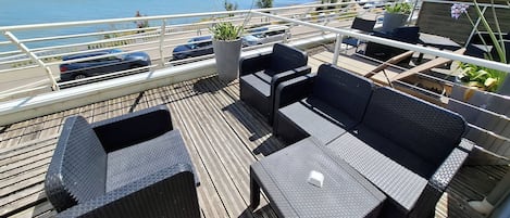 A deck with wicker furniture, a potted plant, and a view of the sea.