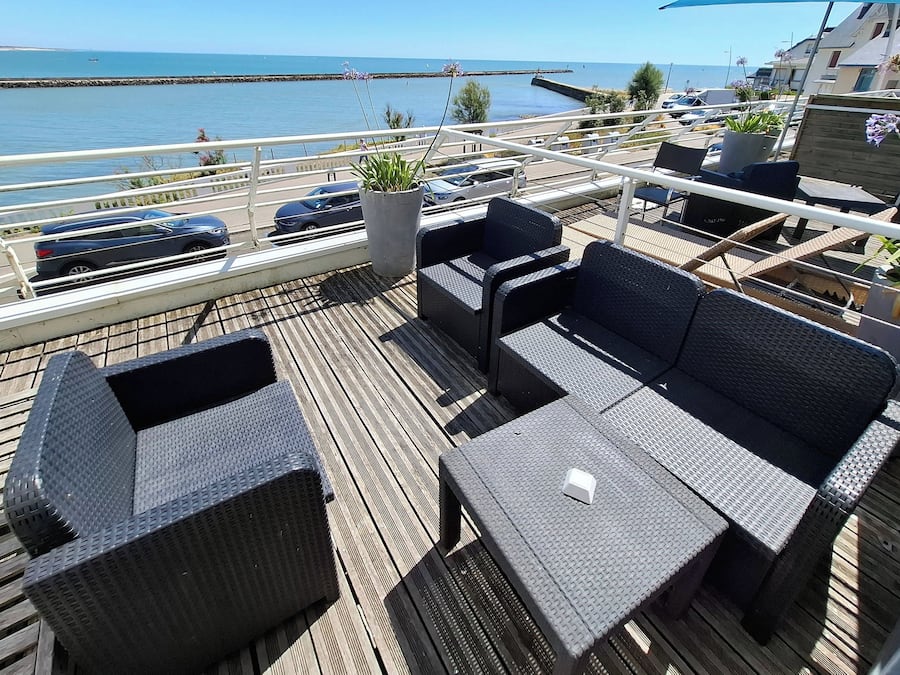 A deck with wicker furniture, a potted plant, and a view of the sea.