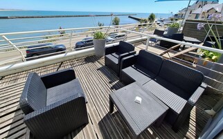Une terrasse dotée de meubles en osier, d’une plante en pot et offrant une vue sur la mer.