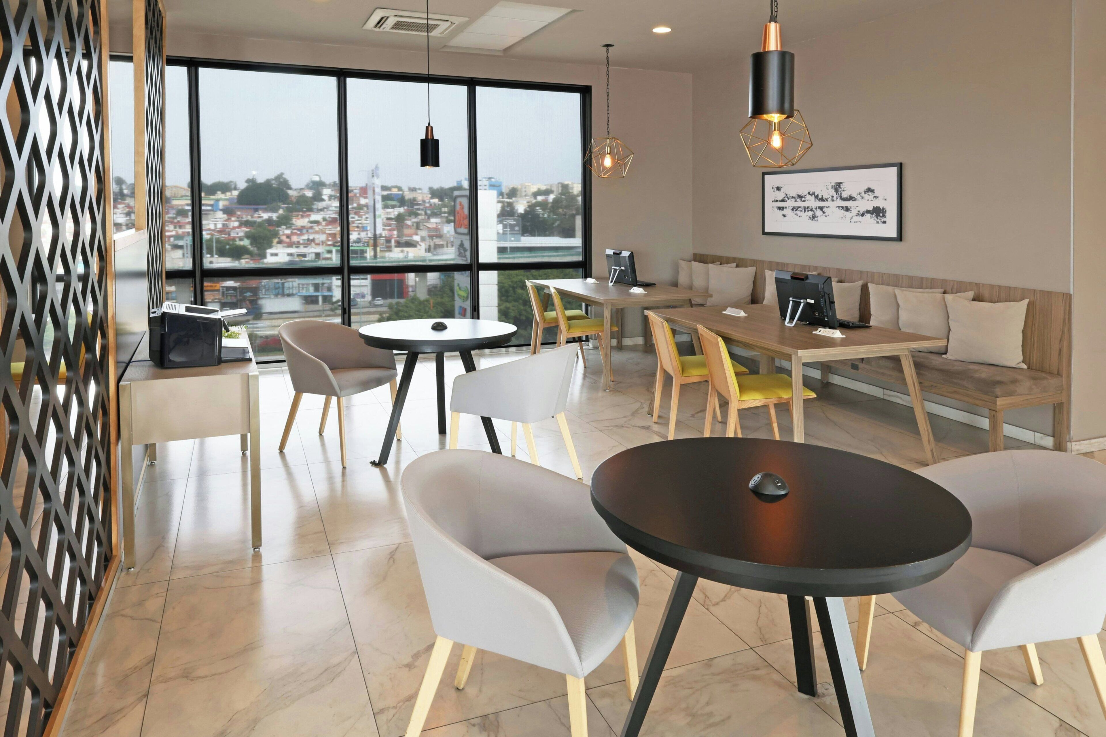 A modern dining area with round tables, grey chairs, and a wooden bench.