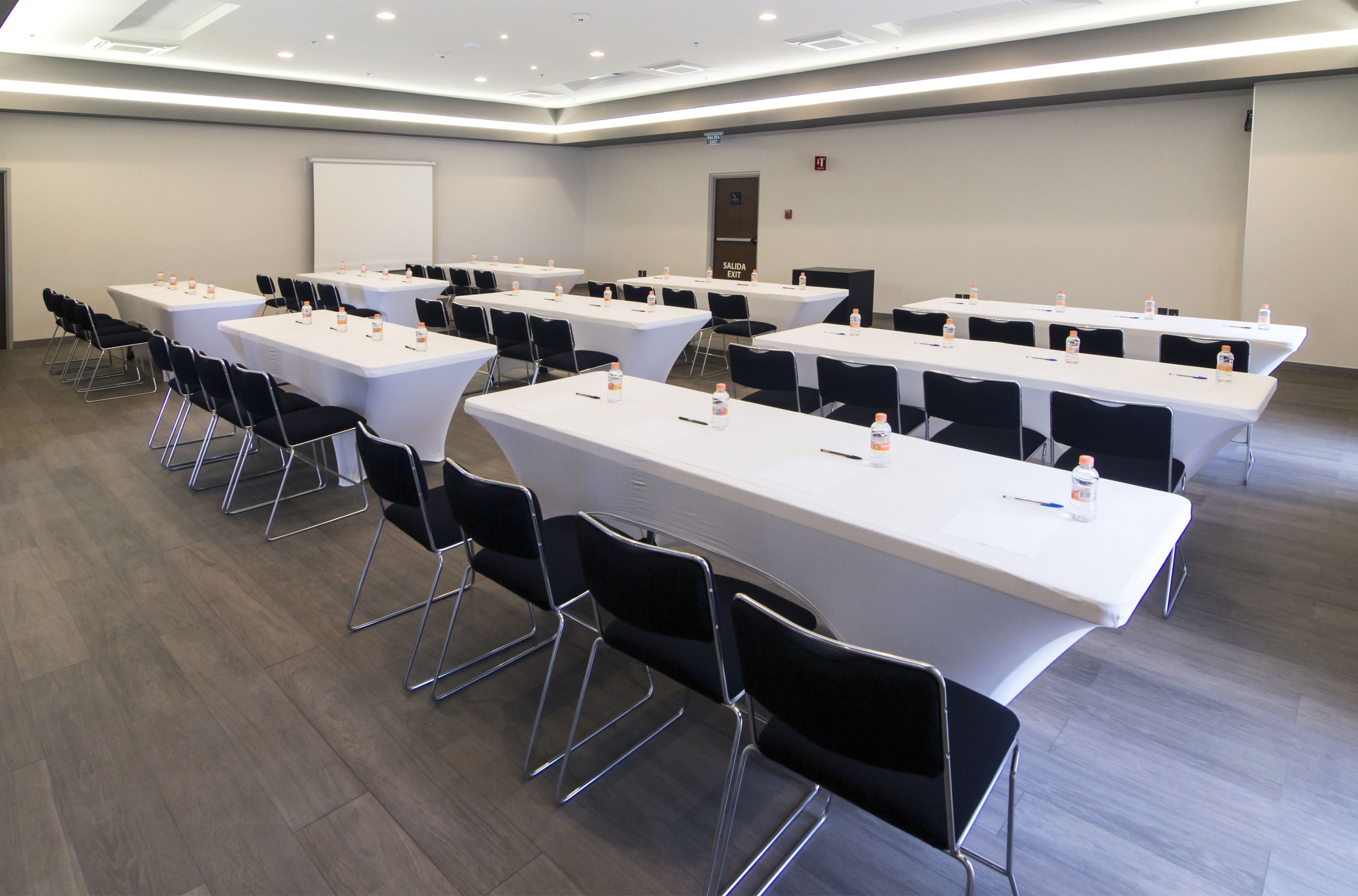 A conference room with multiple tables and chairs, equipped with water bottles and pens.