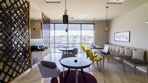 A modern office space with a round table, chairs, a sofa, and a view of the city through large windows.