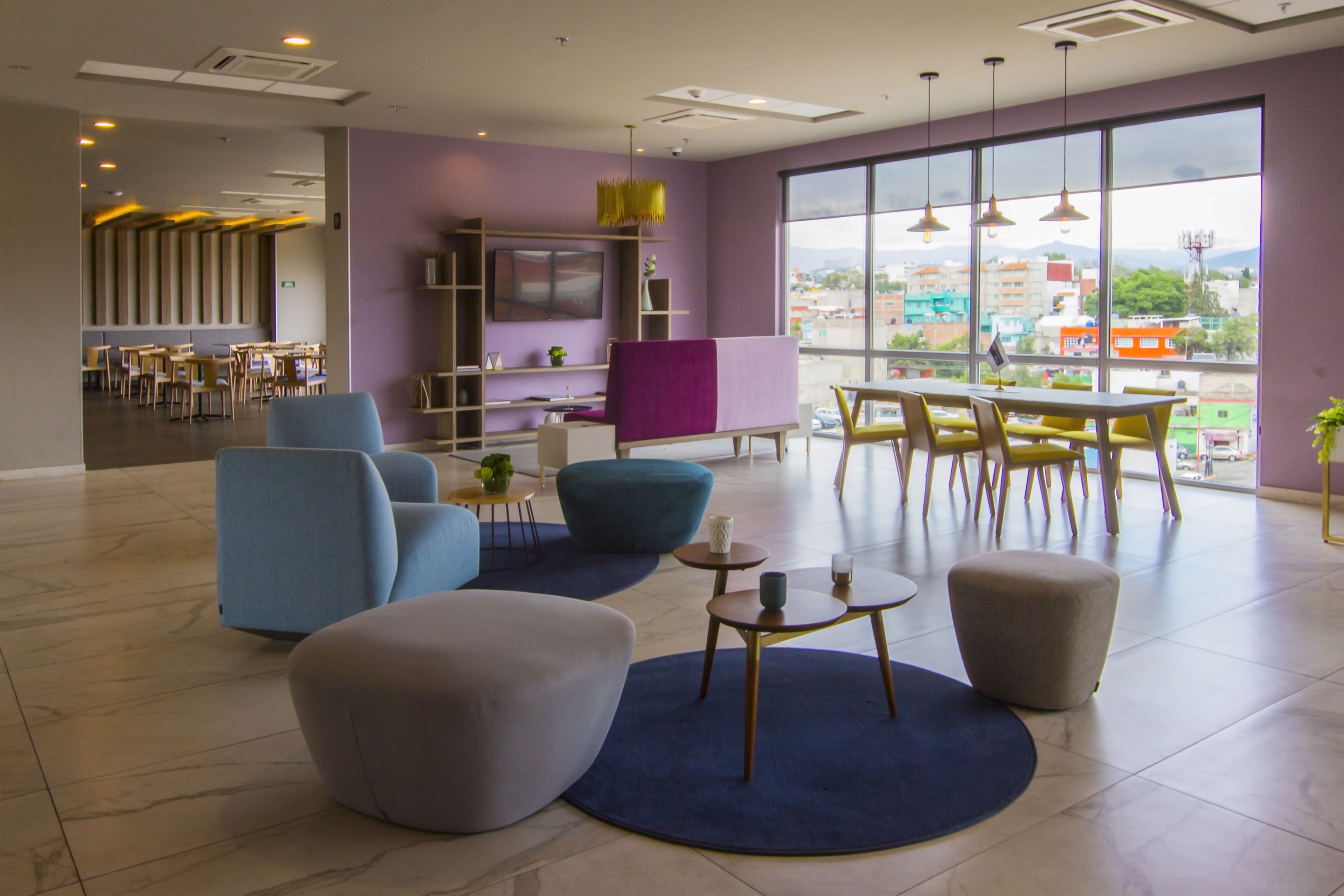 A modern lounge area with seating, a dining area, and large windows offering a city view.