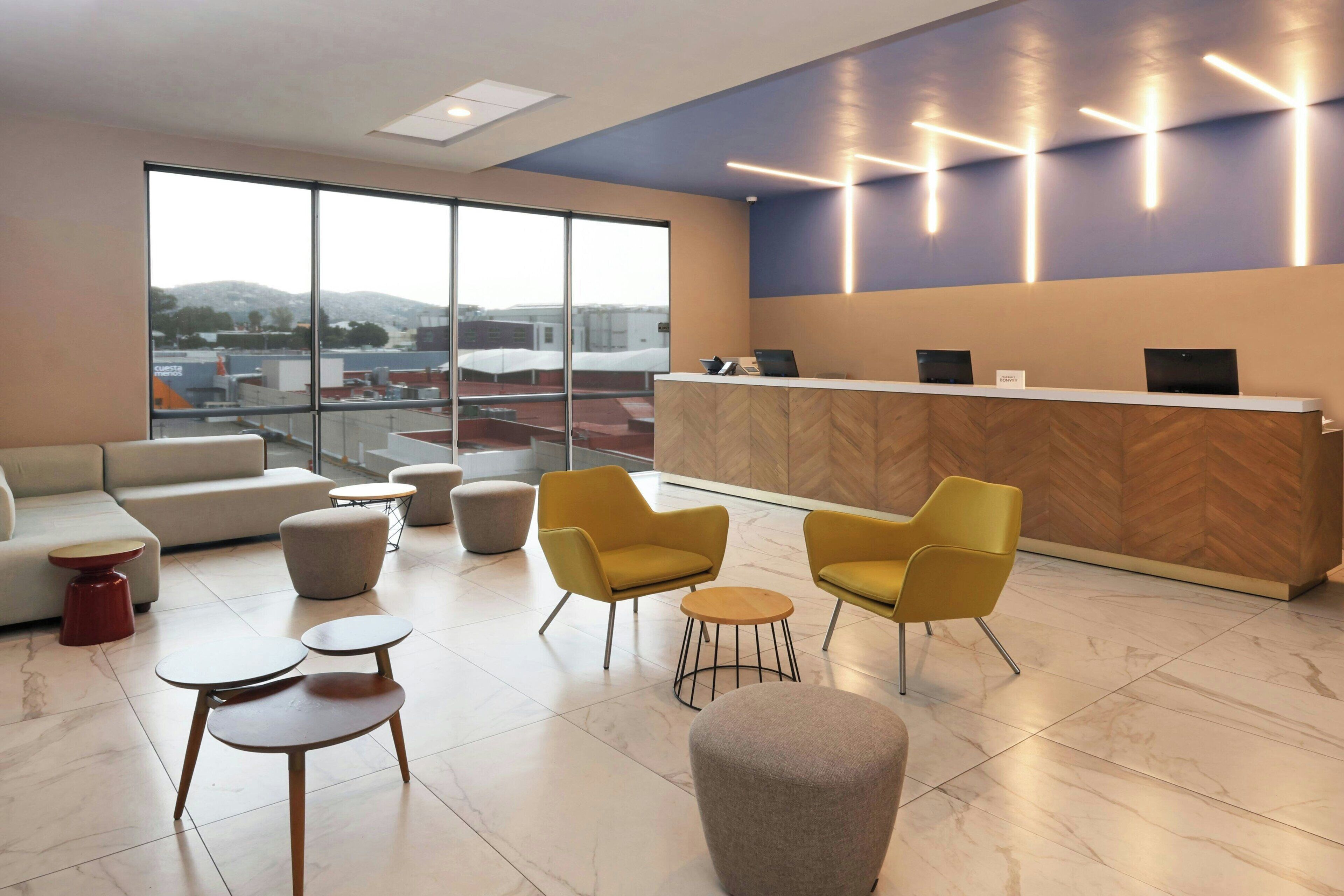 A modern reception area with a wooden reception desk, yellow chairs, and a large window offering a city view.