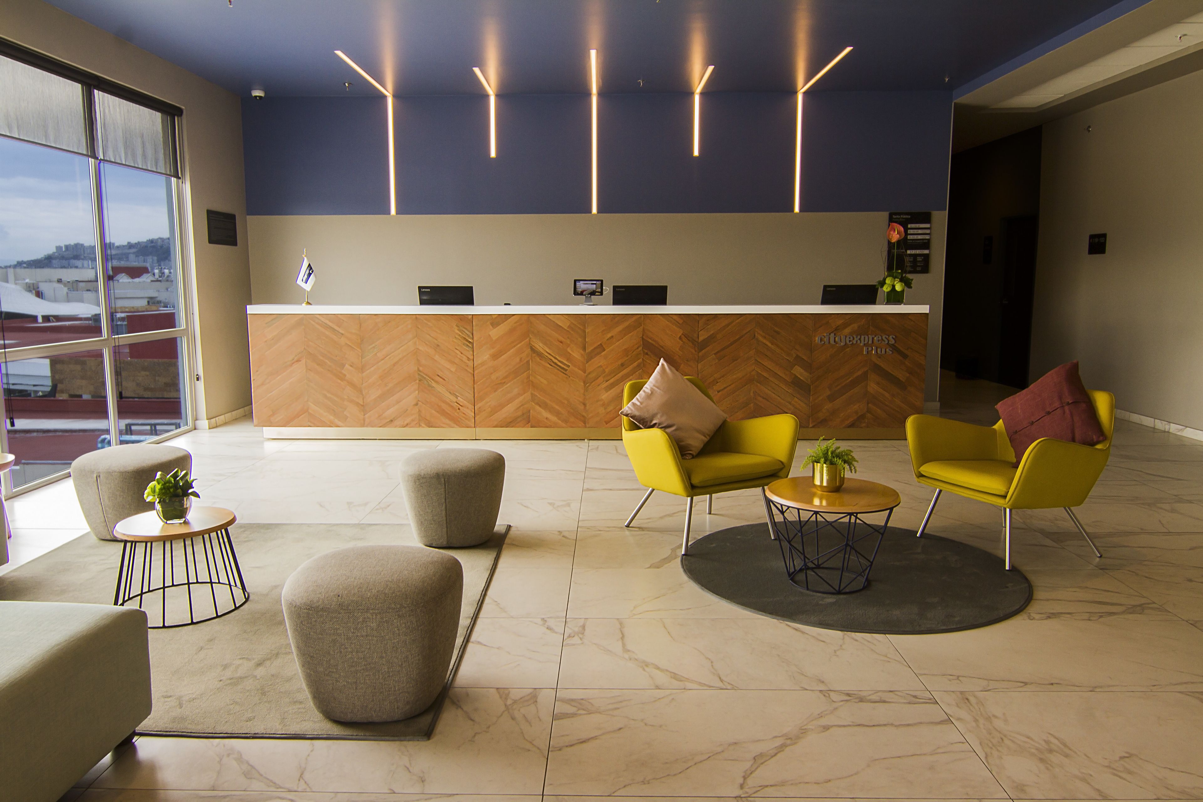 A modern reception area with a herringbone wood panel wall, a reception desk, and seating arrangements including a yellow armchair and a grey ottoman.
