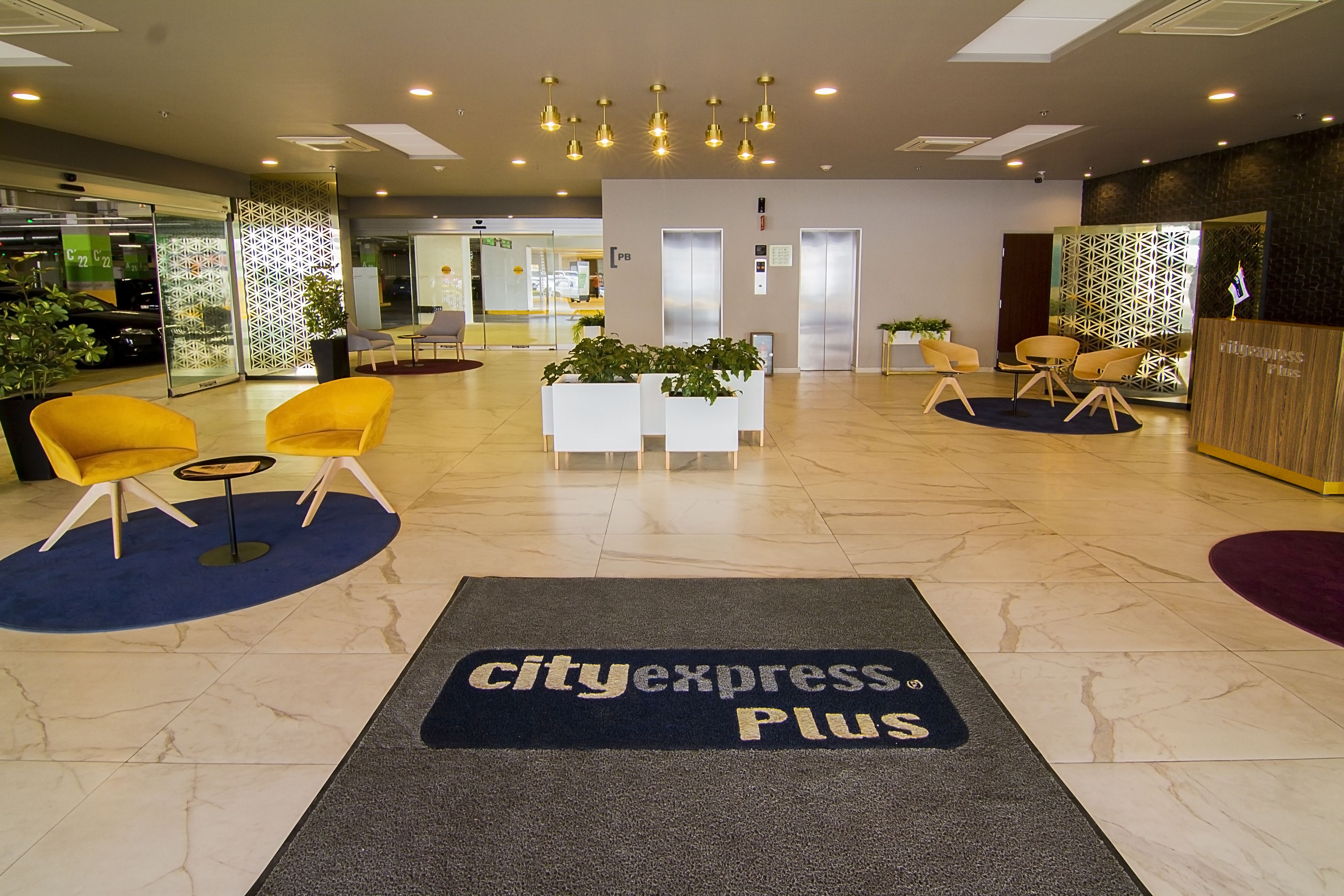 A hotel lobby with a reception desk, seating area, and a 'CityExpress Plus' carpet.