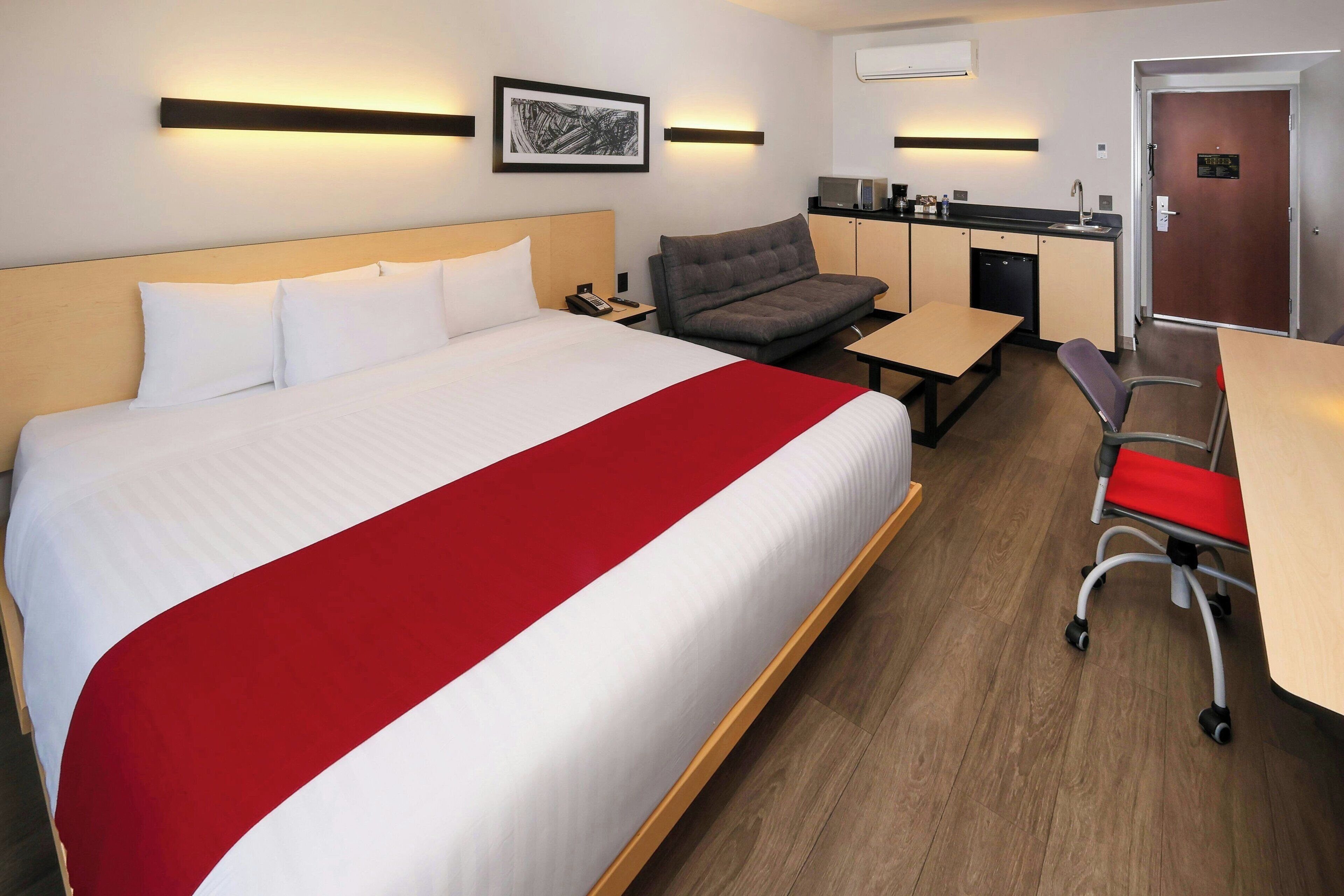 Ein Hotelzimmer mit einem großen Bett, einem Schreibtisch, einer Couch und einer Küchenzeile.
