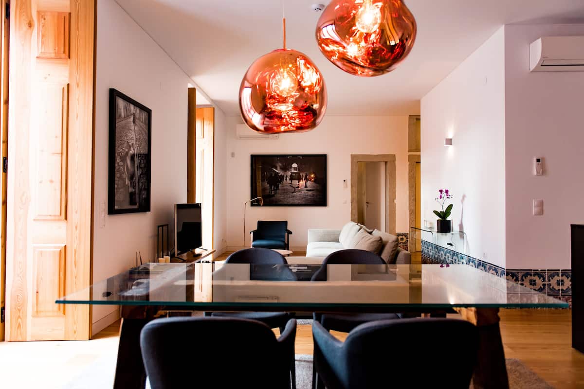 A modern living room with a glass dining table, black chairs, a sofa, and two pendant lights.