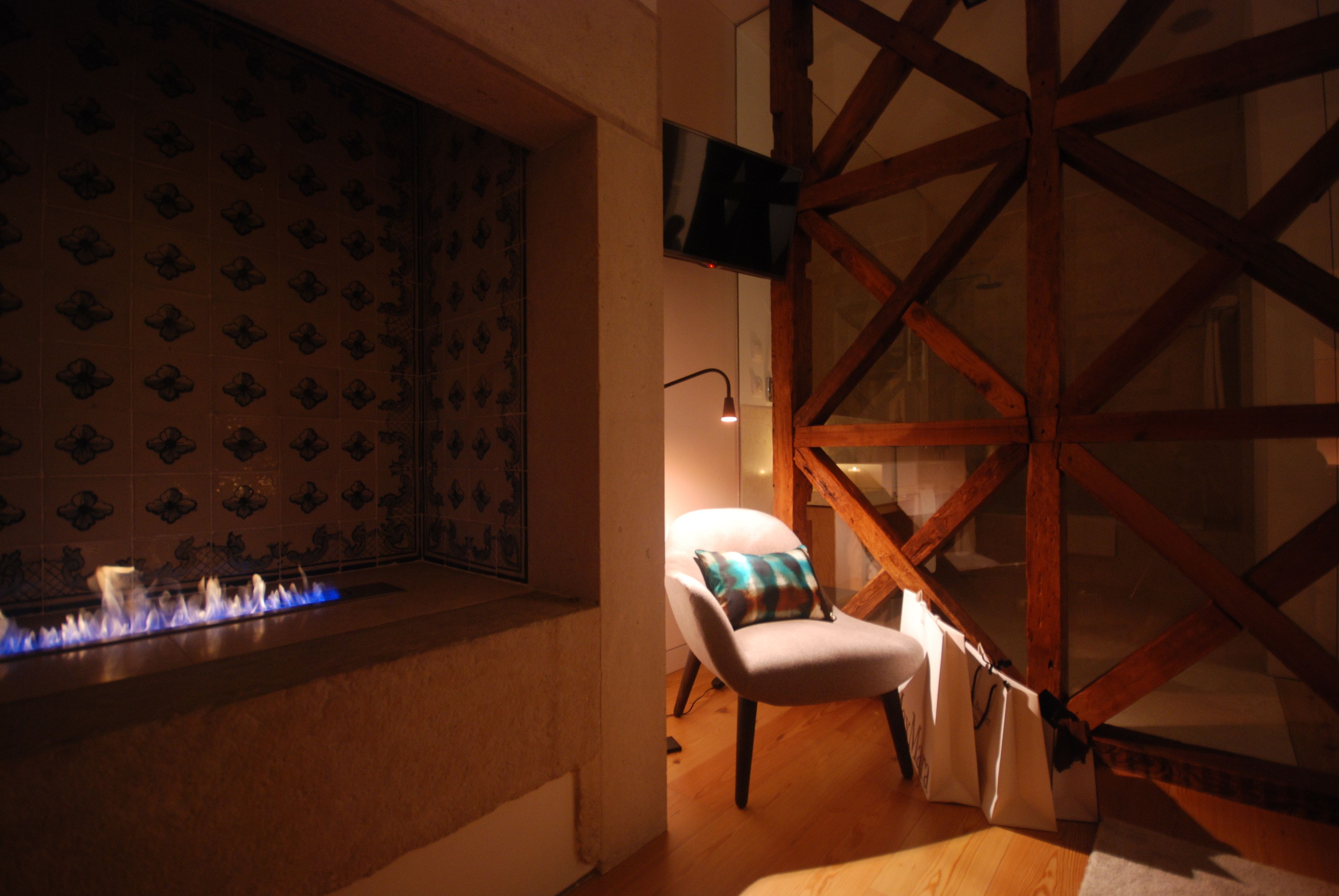 Een kamer met een open haard, een stoel met een kussen en een zichtbare houten balkenstructuur.
