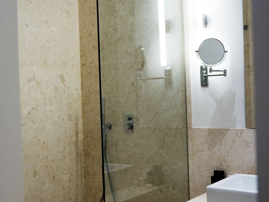 A modern bathroom with a glass-enclosed shower, a white sink, and a mirror with a round frame.