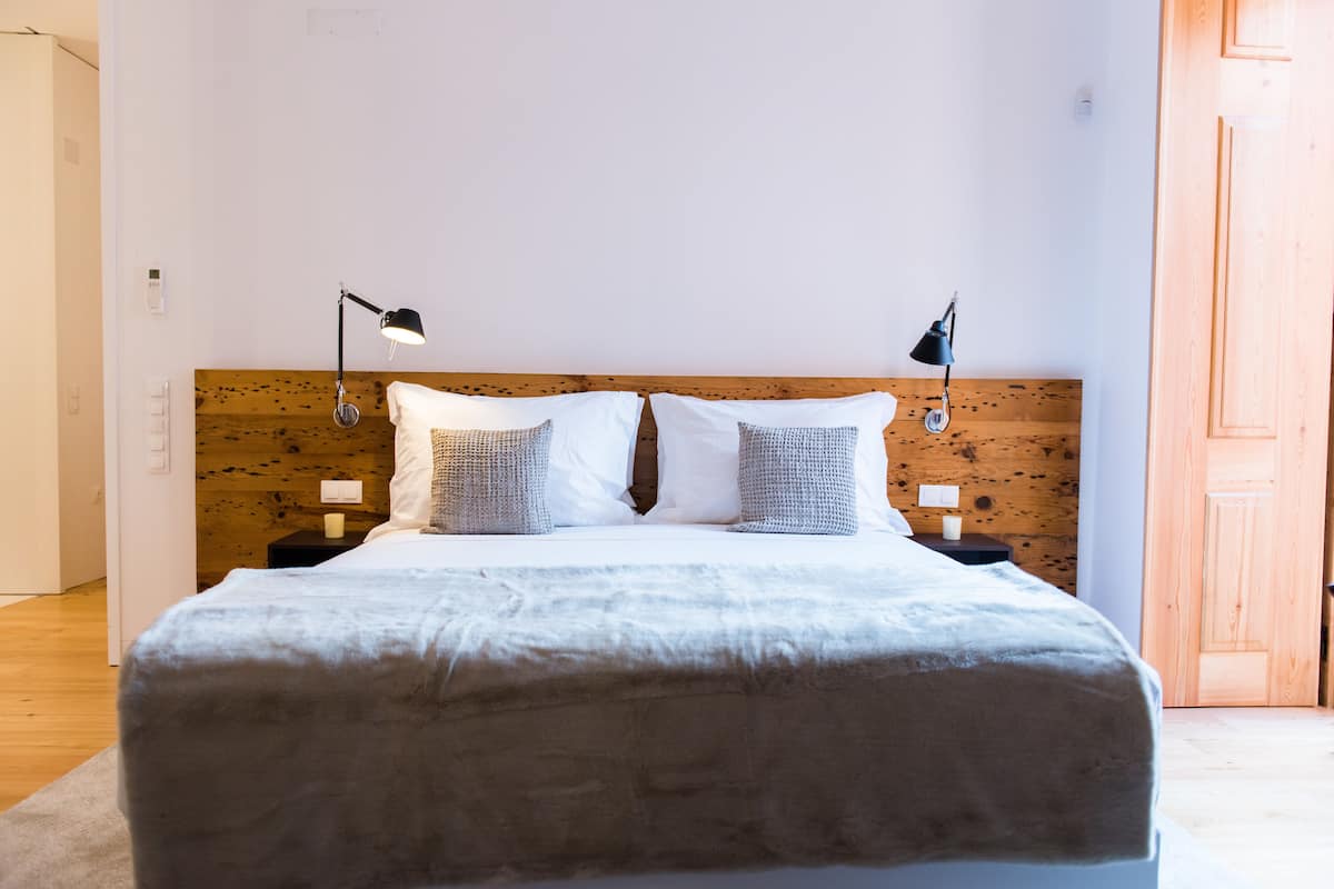 A neatly made bed with a wooden headboard, two bedside lamps, and a white pillow.