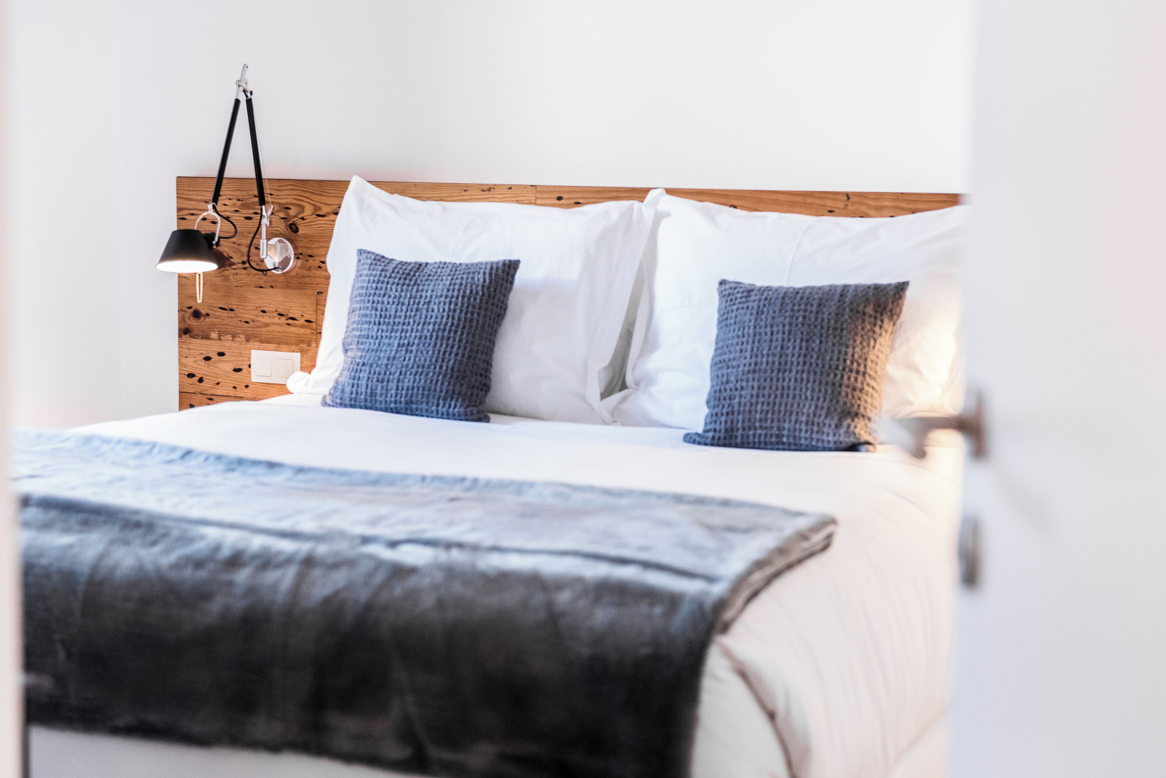 Uma cama bem arrumada com um cobertor branco e azul, duas almofadas e um abajur ao lado.
