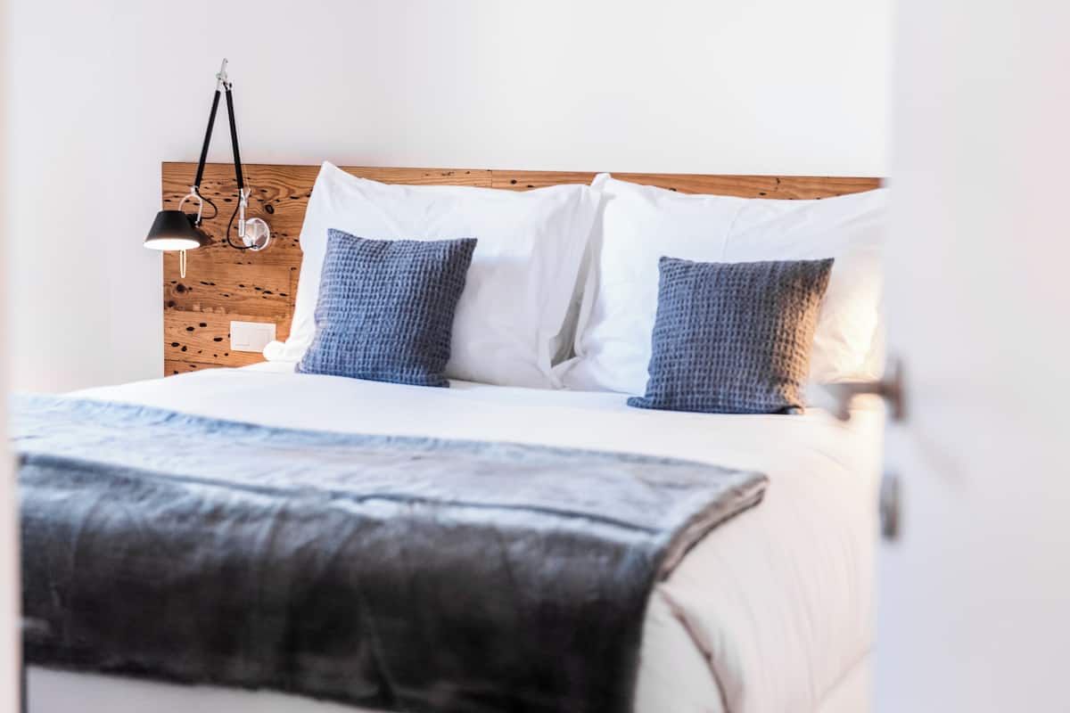 A neatly made bed with a white and blue blanket, two pillows, and a bedside lamp.