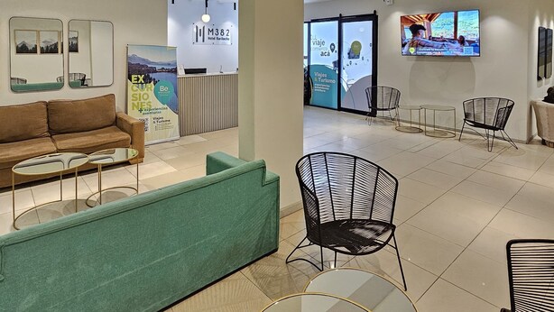 A modern hotel lobby with a sofa, chairs, a TV, and a reception desk.