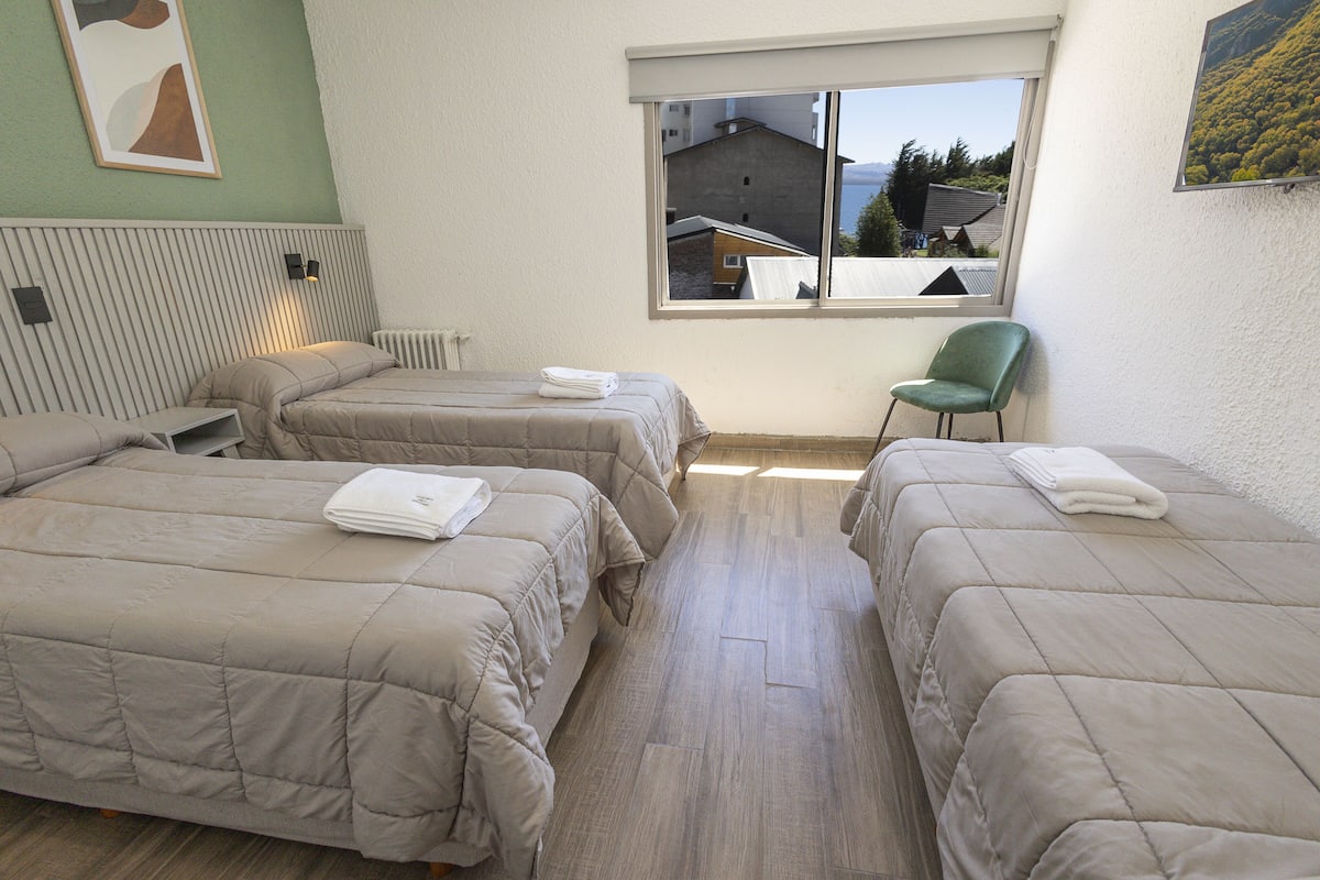 A room with two beds, a chair, and a window with a view of buildings.