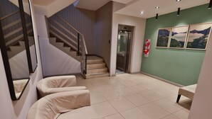 A hotel lobby with a staircase, a reception desk, and three beige armchairs.